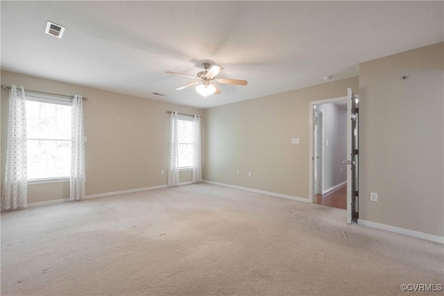 spare room featuring a healthy amount of sunlight, light colored carpet, a ceiling fan, and visible vents