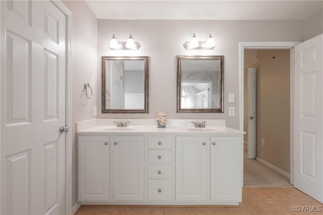 bathroom with baseboards, tile patterned flooring, double vanity, and a sink