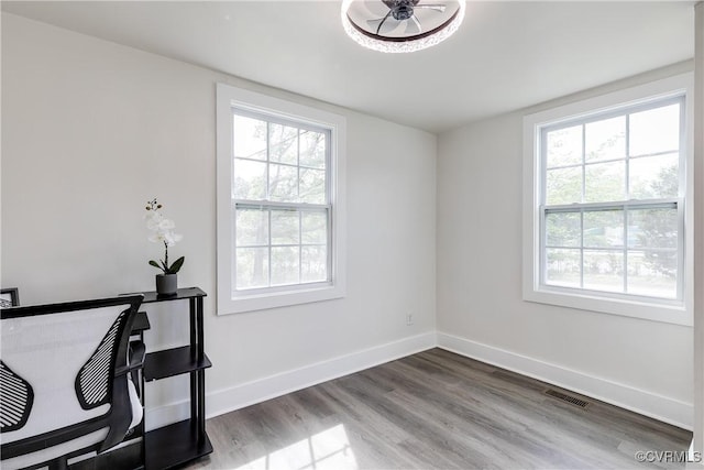 interior space featuring baseboards, visible vents, a healthy amount of sunlight, and wood finished floors