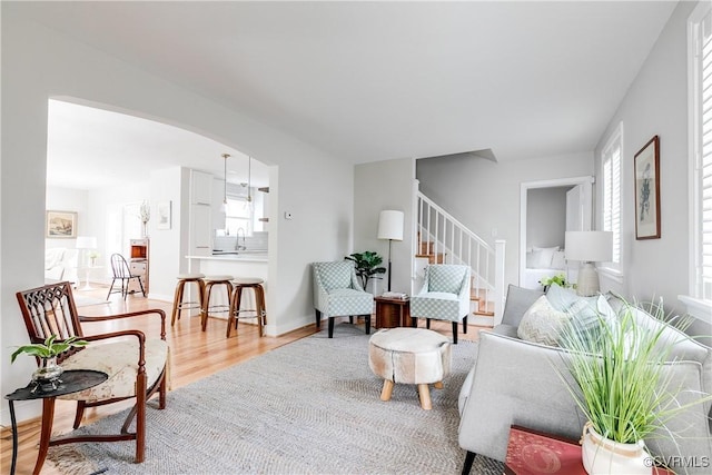 living area featuring light wood finished floors, arched walkways, and stairs