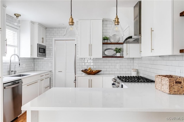 kitchen featuring open shelves, a sink, appliances with stainless steel finishes, light countertops, and wall chimney exhaust hood