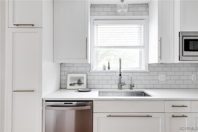 kitchen with tasteful backsplash, white cabinets, a sink, stainless steel appliances, and light countertops