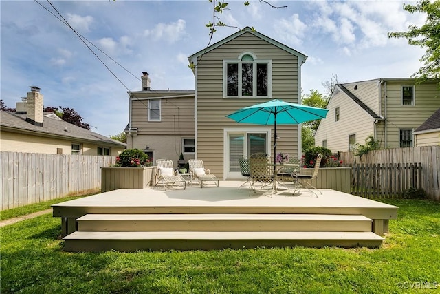 rear view of property featuring a deck, fence, and a lawn