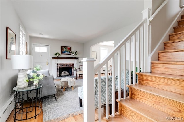 stairway featuring wood finished floors, arched walkways, baseboard heating, and a brick fireplace