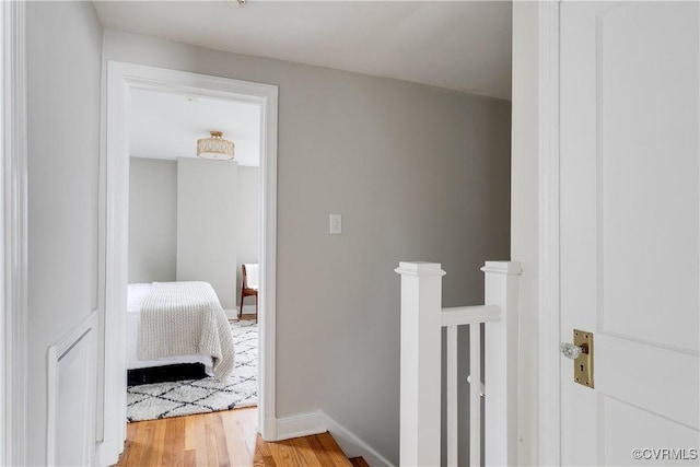 hallway with light wood-style floors, baseboards, and an upstairs landing