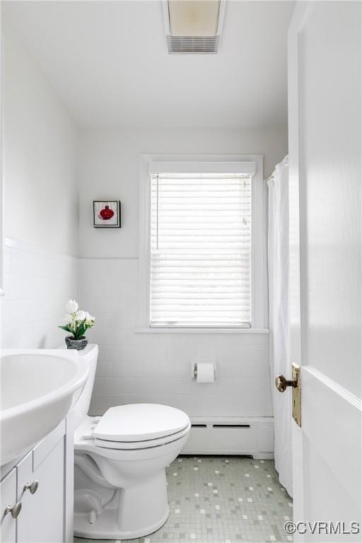 bathroom with a baseboard radiator, tile walls, toilet, vanity, and visible vents