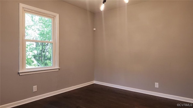 spare room featuring baseboards, a healthy amount of sunlight, and dark wood-type flooring