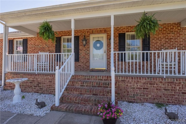doorway to property featuring covered porch and brick siding