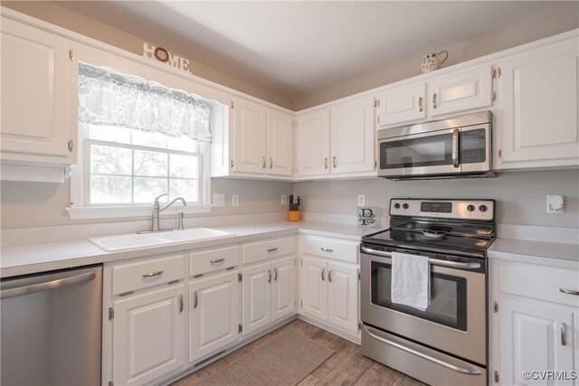 kitchen featuring white cabinetry, a sink, appliances with stainless steel finishes, light wood-style floors, and light countertops