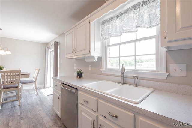 kitchen featuring a sink, white cabinetry, light countertops, stainless steel dishwasher, and wood finished floors