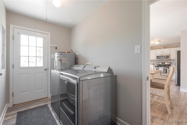 washroom featuring washing machine and dryer, baseboards, water heater, light wood-type flooring, and laundry area