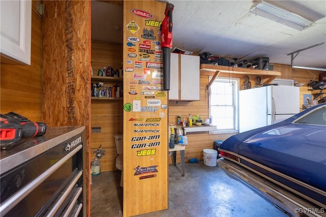 garage with wood walls and freestanding refrigerator