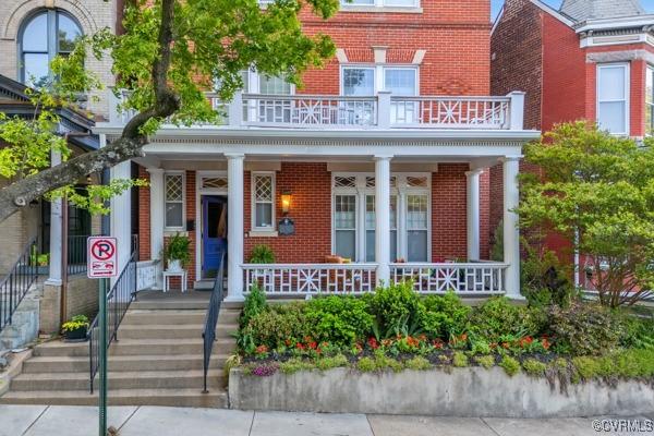 exterior space featuring a balcony, covered porch, and brick siding
