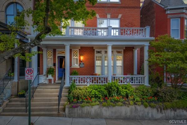 entrance to property with covered porch, brick siding, and a balcony