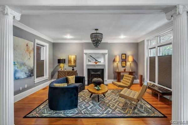 living room with crown molding, baseboards, ornate columns, and wood finished floors