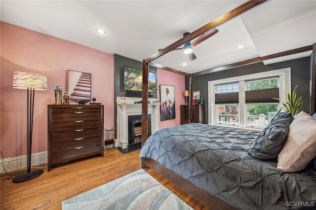 bedroom featuring recessed lighting, baseboards, a glass covered fireplace, and wood finished floors