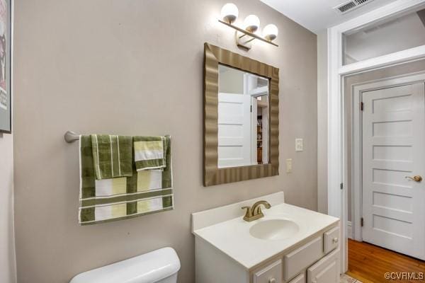 half bath featuring toilet, visible vents, wood finished floors, and vanity