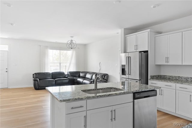 kitchen featuring a kitchen island with sink, light wood-type flooring, white cabinets, a sink, and appliances with stainless steel finishes
