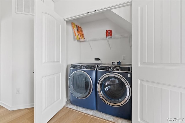 clothes washing area with laundry area, baseboards, wood finished floors, visible vents, and washer and clothes dryer
