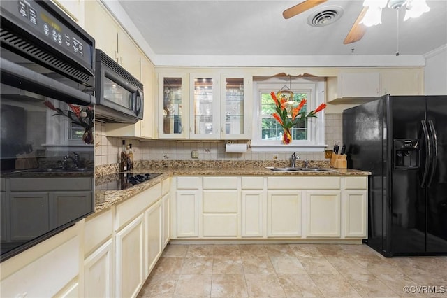 kitchen with decorative backsplash, a sink, visible vents, black appliances, and light stone countertops