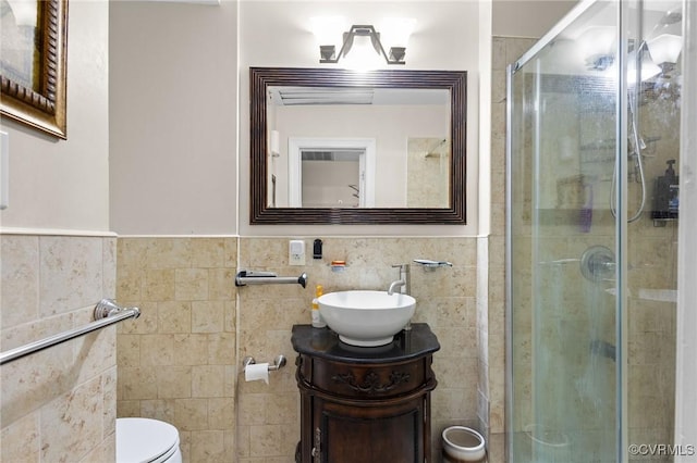 bathroom with wainscoting, a shower stall, tile walls, toilet, and vanity
