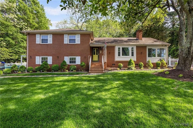 tri-level home featuring brick siding, fence, a front yard, and a chimney