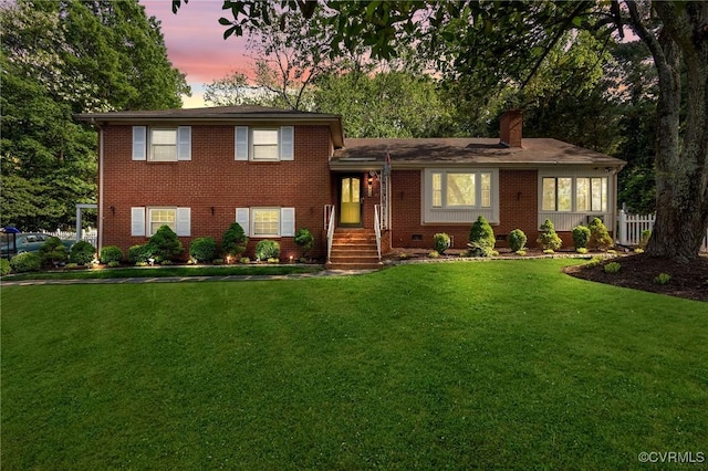 tri-level home featuring a chimney, brick siding, fence, and a front lawn
