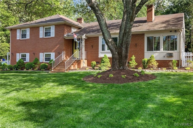 tri-level home featuring a chimney, brick siding, and a front lawn