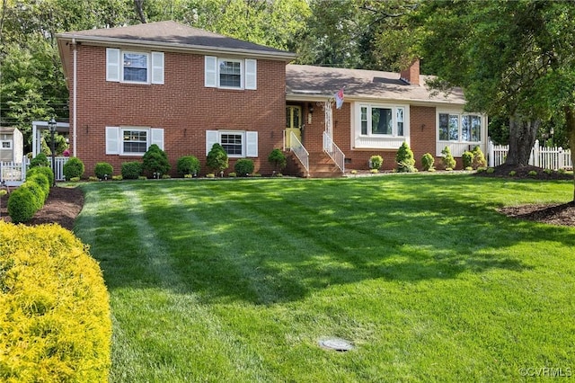 tri-level home with fence, a chimney, a front yard, and brick siding