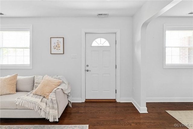 entryway featuring dark wood-type flooring, arched walkways, baseboards, and visible vents