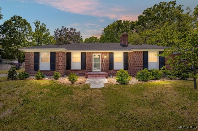 ranch-style house featuring a lawn, a chimney, and brick siding