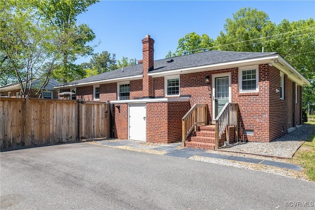 view of front of home featuring crawl space, a chimney, roof with shingles, brick siding, and fence