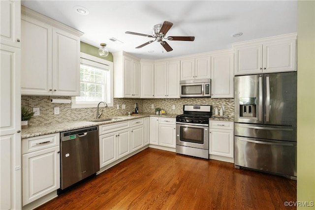 kitchen with light stone counters, a sink, stainless steel appliances, a ceiling fan, and backsplash