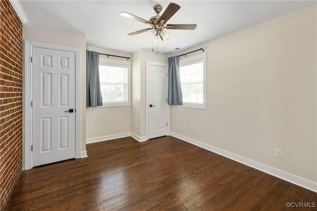 unfurnished bedroom with baseboards, ceiling fan, wood finished floors, and brick wall