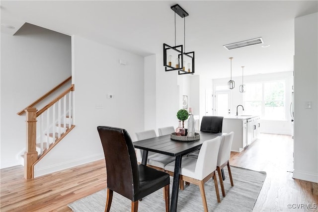 dining area featuring an inviting chandelier, light wood finished floors, stairs, baseboards, and visible vents