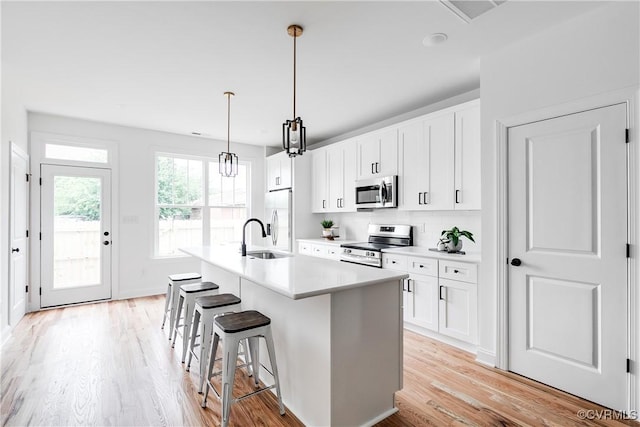 kitchen featuring a kitchen breakfast bar, a sink, light wood-style floors, stainless steel appliances, and an island with sink