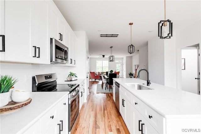 kitchen with decorative light fixtures, appliances with stainless steel finishes, light wood-type flooring, a sink, and white cabinets