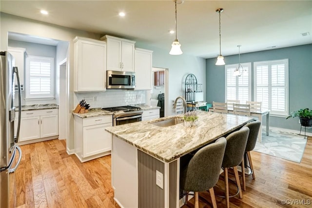 kitchen with light stone countertops, a sink, light wood-style flooring, stainless steel appliances, and white cabinetry