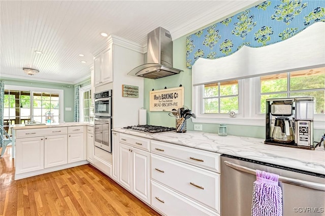 kitchen featuring crown molding, light wood-type flooring, wall chimney exhaust hood, white cabinetry, and stainless steel appliances