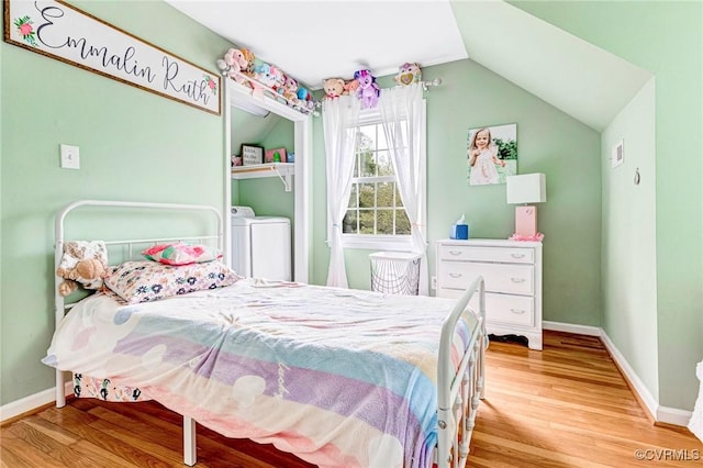 bedroom featuring baseboards, wood finished floors, vaulted ceiling, and washing machine and clothes dryer