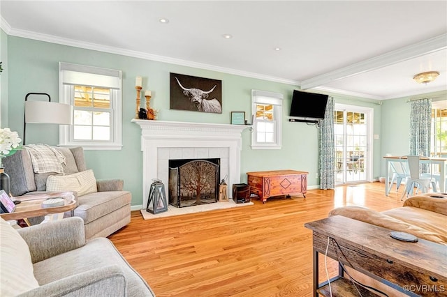 living area with light wood-type flooring, baseboards, crown molding, and a tiled fireplace