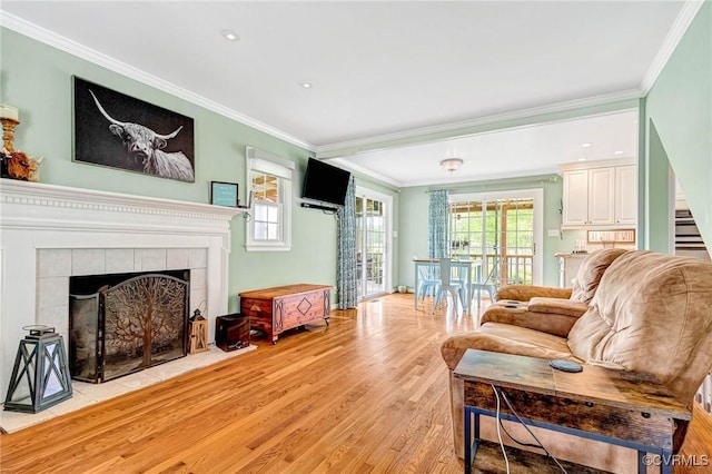 living room with light wood-style floors, ornamental molding, a tiled fireplace, and stairway