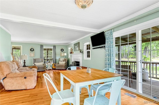 dining room featuring crown molding, a fireplace, light wood-style flooring, and visible vents