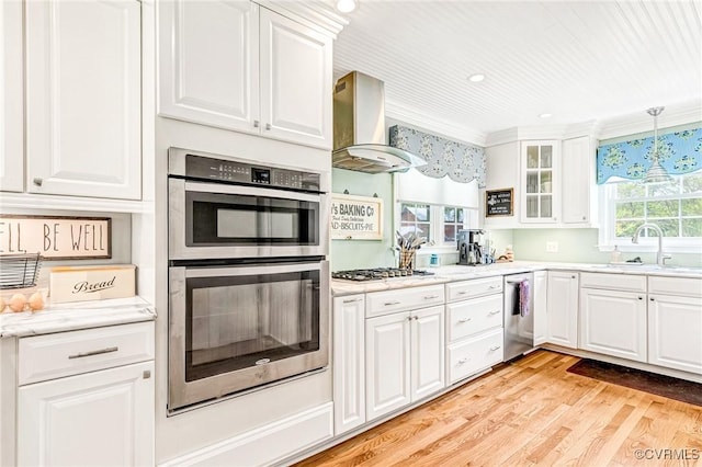 kitchen featuring a sink, wall chimney exhaust hood, stainless steel appliances, white cabinetry, and light wood-type flooring