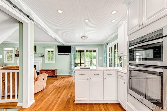 kitchen featuring crown molding, white cabinetry, double oven, a peninsula, and light wood-style flooring