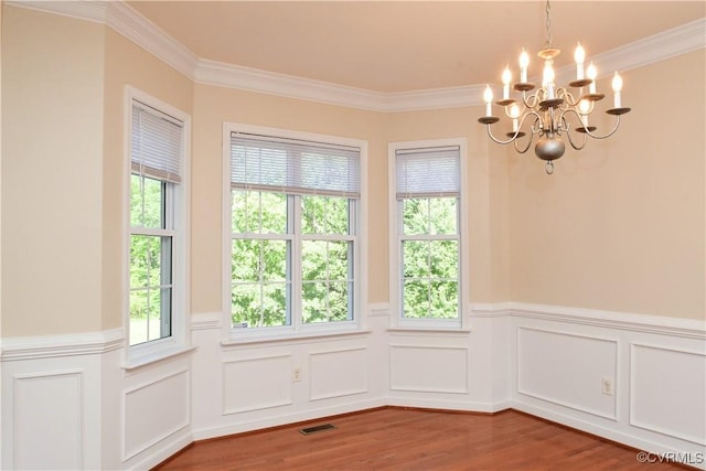 unfurnished dining area featuring visible vents, crown molding, wood finished floors, a wainscoted wall, and a chandelier