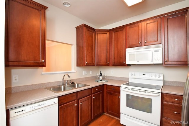 kitchen with a sink, wood finished floors, white appliances, and light countertops