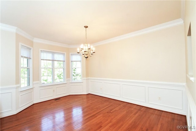 unfurnished dining area featuring a notable chandelier, ornamental molding, wood finished floors, and a wainscoted wall