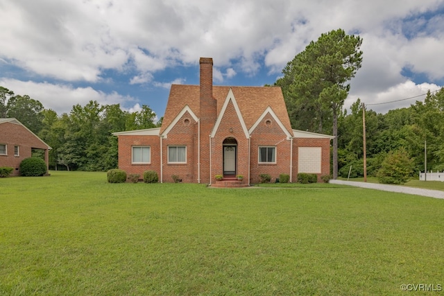 tudor house with driveway, a chimney, brick siding, a front lawn, and an attached garage