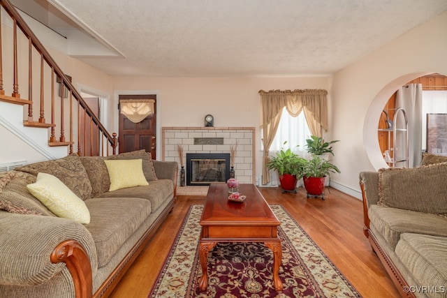 living room with a textured ceiling, light wood finished floors, stairs, and a fireplace